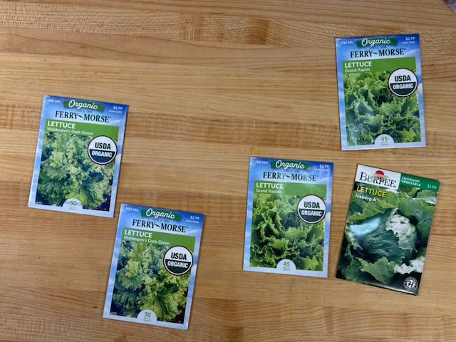 Five packages of 'Green Wave' lettuce seeds on a wooden surface